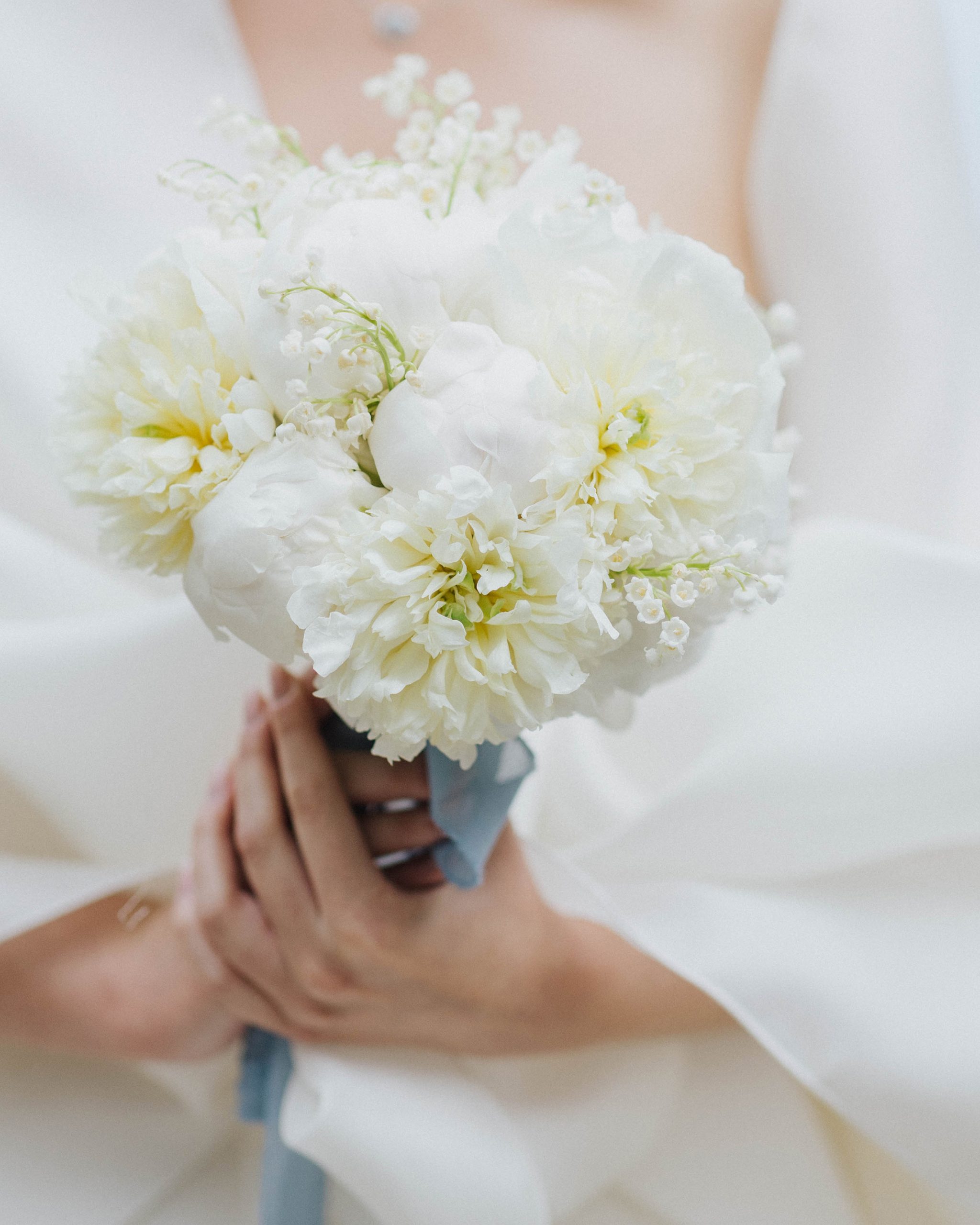 White round bridal bouquet with peonies and lily of the valley and dusty blue ribbon